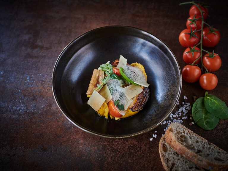 Ein Teller ist mit einer leckeren Speise gefüllt und mit Tomaten und Brot in Szene gesetzt